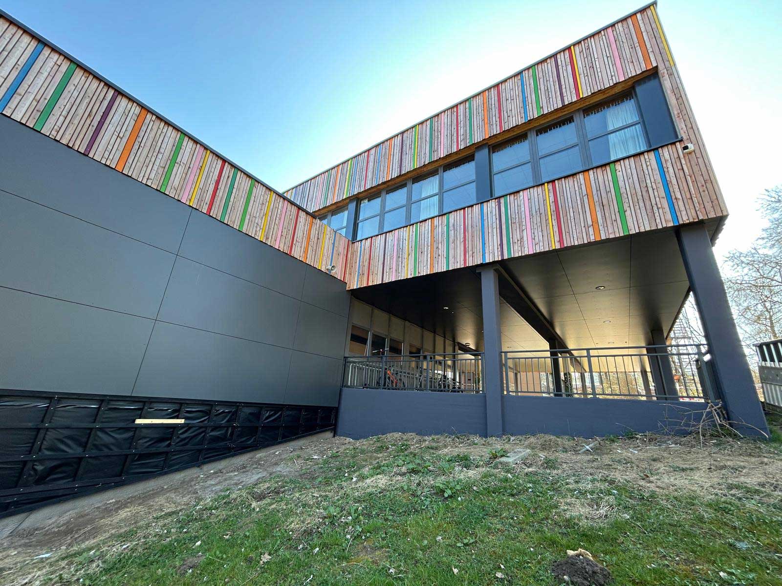 Modernes Gebäude mit Holzfassade und farbigen Akzentleisten, aufgenommen aus der Untersicht.